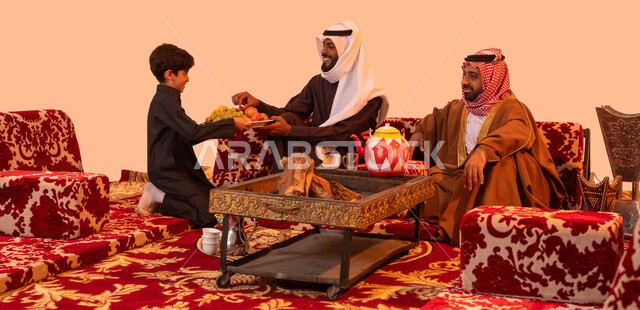 تبادل الأحاديث والقصص مع الأصدقاء، استقبال الضيوف بابتسامة وترحيب، بورتريه لولد عربي خليجي سعودي يقوم بتقديم الفاكهة للضيف، جلسات سعودية تقليدية في الهواء الطلق، مفهوم الكشتة البرية، خلفية بيج