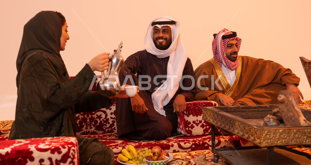 جلسات بدوية تقليدية، الاجتماع حول الموقد الطيني للتدفئة، العادات والتقاليد التراثية في إكرام الضيف، نزهة برية في الصحراء، مفهوم حسن الضيافه والاستقبال، بورتريه لإمرأة عربية خليجية سعودية تستخدم دلة نحاسية لصب القهوة، خلفية بيج.