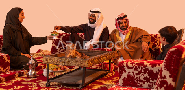 الاجتماع حول الموقد الطيني للتدفئة، وجبة ذات قيمة غذائية عالية، نزهة برية في الصحراء، رحلات تخييم سياحية ترفيهية، مفهوم حسن الضيافه والاستقبال، بورتريه لإمرأة عربية خليجية سعودية تقوم بتقديم التمر للضيوف في جلسة خارجية، خلفية بيج.