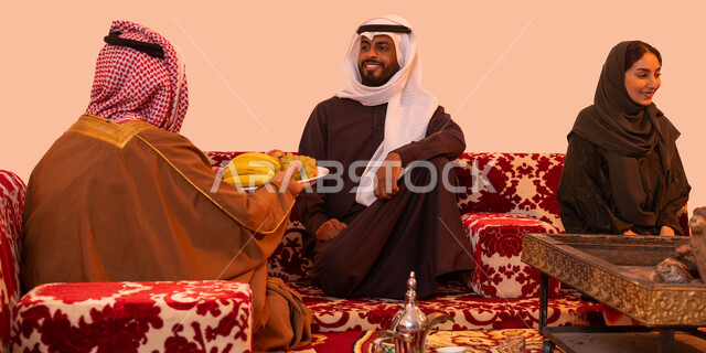 العادات والتقاليد السعودية العريقة في إكرام الضيف، نزهة برية في الصحراء، رحلات تخييم سياحية ترفيهية، إيماءات البشاشة والترحيب، مفهوم حسن الضيافه والاستقبال، التسامر وتبادل الأحاديث في كشتة شعبية، بورتريه لرجل عربي سعودي خليجي يقوم بتقديم الفاكهة للضيوف، خلفية بيج.