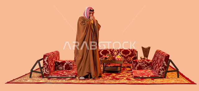 Recreational wild kashta, the cold winter atmosphere in camping places, the feeling of frost and extreme cold, a portrait of a Saudi Gulf Arab man wearing the traditional bisht and shemagh and placing his hands on his shoulder in a crossed manner, full-length body image, beige background