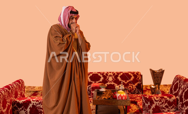 الشعور بالبرد والصقيع, جلسة بر شبابية شعبية، أسلوب الحياة البدوية القديمة, مخيمات وأجواء شتوية، بورتريه مقرب لرجل عربي خليجي سعودي يرتدي الشماغ التقليدي يتنفس في يديه لتبقى دافئة ، الأجواء الهادئة في أماكن التخييم، خلفية بيج.
