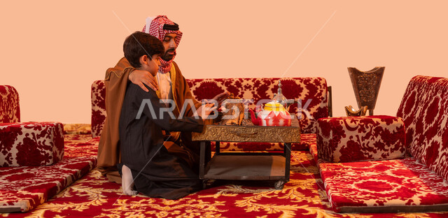أساليب الحياة القديمة, إيماءات التدفئة على الموقد, مخيمات وأجواء شتوية، بورتريه لأب عربي خليجي سعودي مبتسم يحتضن ولده بإيماءات العطف والحنان، الاستمتاع في قضاء أوقات مع الأبناء،  كشتة بر أسرية ترفيهية، خلفية بيج.