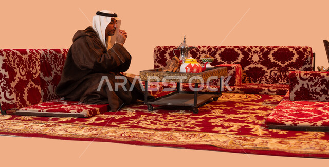 النفخ داخل الكفين للشعور بالدفئ، الأجواء الهادئة في المخيمات الشعبيه ،إيماءات التدفئة على الموقد, جلسة بر شبابية شعبية، بورتريه لرجل كبير السن عربي خليجي سعودي يرتدي الزي التقليدي والملابس الشتوية الدافئة يجلس أمام شعلة من النار ، خلفية بيج