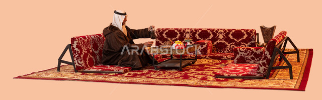 جلسة شعبيه في البراري ،نزهه بريه في الصحراء، عادات وتقاليد سعودية اصيلة في تقديم القهوة العربية، مفهوم حسن الضيافه والكرم، بورتريه لرجل مسن عربي خليجي سعودي مبتسم يرتدي الزي التقليدي والملابس الشتوية الدافئة يقوم بصب القهوة باستخدام الدلة النحاسية، خلفية بيج