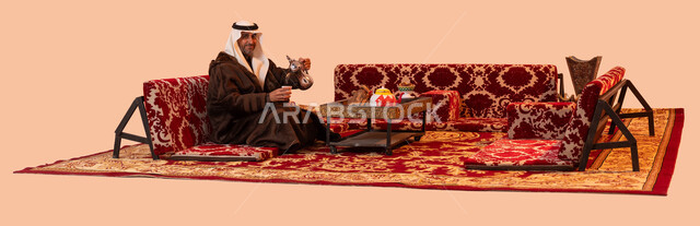 عادات وتقاليد سعودية اصيلة في تقديم القهوة العربية، مفهوم حسن الضيافه والكرم، جلسات شعبية خارجية شبابية، بورتريه لرجل كبير السن عربي خليجي سعودي مبتسم يرتدي الزي التقليدي والملابس الشتوية الدافئة يقوم بصب القهوة باستخدام الدلة النحاسية، خلفية بيج.