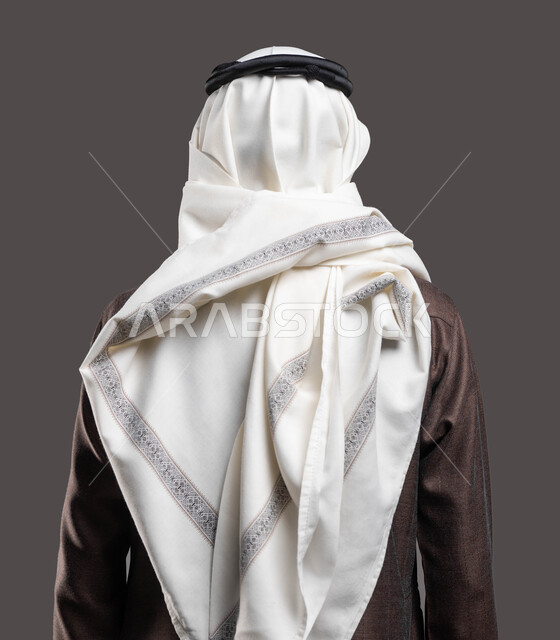 الوقوف بثقة واستقامة، بورتريه مقرب من الخلف لرجل عربي خليجي سعودي يرتدي الزي التقليدي والشماغ ، مفهوم الاناقة والاهتمام بالمظهر الخارجي، خلفية رمادية