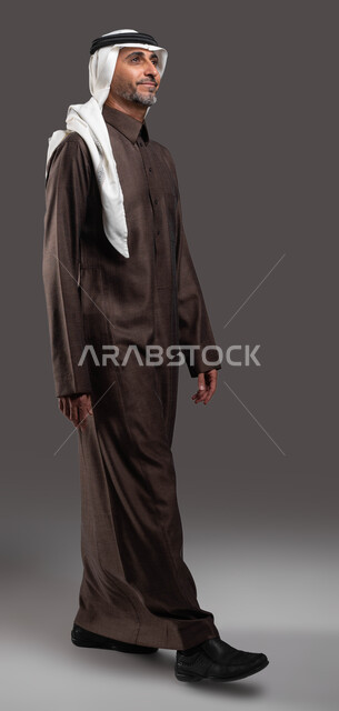 ايماءات المشي و الذهاب إلى مكان معين،  بورتريه لرجل كبير السن عربي خليجي سعودي مبتسم يرتدي الزي التقليدي ينظر إلى شيء ما، التقدم إلى الأمام بخطوات ثابتة، صورة الجسم بالطول الكامل، خلفية رماديه