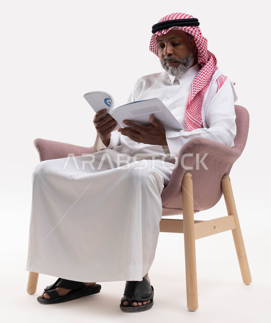 Reading carefully and with concentration, acquiring education and knowledge, spending free time with education and learning, the concept of eradicating illiteracy, a portrait of an elderly Saudi Arabian Gulf man wearing a shemagh and traditional dress, practicing the hobby of reading useful books in his free time, white background.