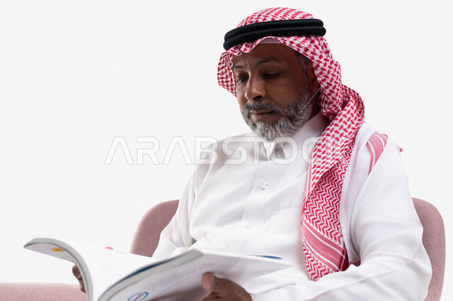 Reading with gestures of contemplation and concentration, acquiring education and knowledge, spending free time with education and learning, the concept of literacy, a close-up portrait of an elderly Saudi Arabian Gulf man wearing a shemagh and traditional dress, practicing the hobby of reading useful books in his free time, white background.