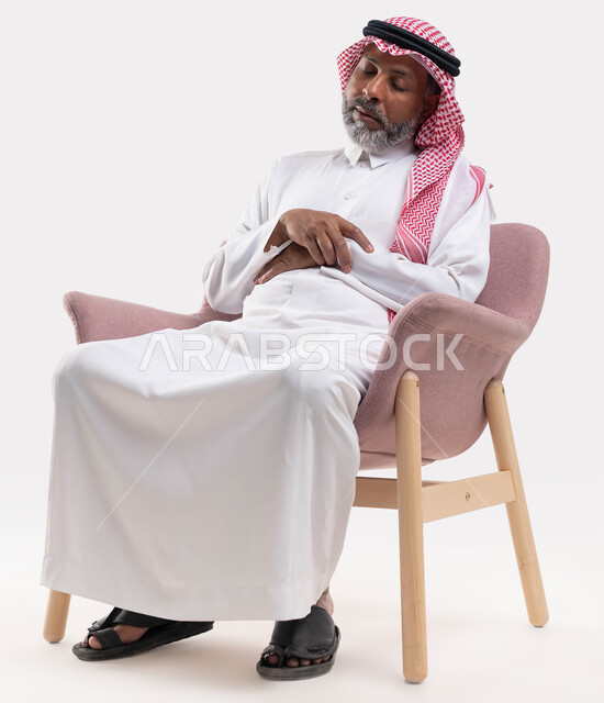 الإحساس بالنعاس باكرا مع تقدم العمر، الحاجة إلى النوم والراحة، الشعور بالتعب والإرهاق، بورتريه لرجل كبير بالسن عربي سعودي خليجي يرتدي الشماغ والثوب التقليدي نائم على الكرسي، خلفية بيضاء