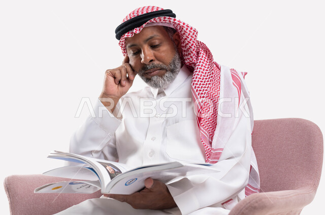 التزود بالعلم والمعرفة، قضاء وقت الفراغ بالتثقيف والتعلم، مفهوم محو الأمية، بورتريه مقرب لرجل كبير بالسن عربي سعودي خليجي يرتدي الشماغ والثوب التقليدي يقرأ كتاب بإيماءات التمعن والتركيز، خلفية بيضاء