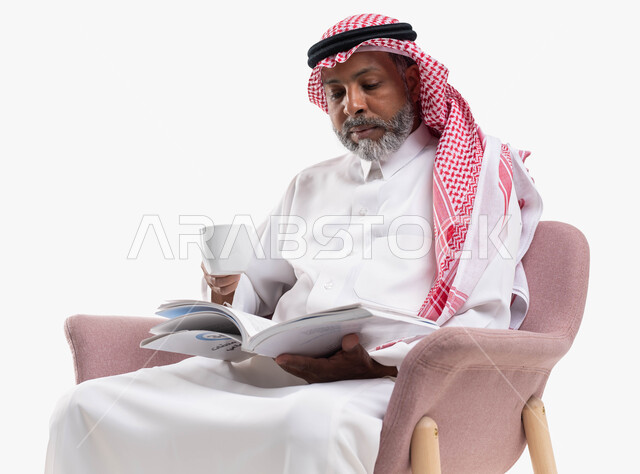 التزود بالعلم والمعرفة، قضاء وقت الفراغ بالتثقيف والتعلم، مفهوم محو الأمية، بورتريه لرجل كبير بالسن عربي سعودي خليجي يرتدي الشماغ والثوب التقليدي يشرب القهوة ويمارس هواية قراءة الكتب المفيدة في وقت الفراغ، خلفية بيضاء