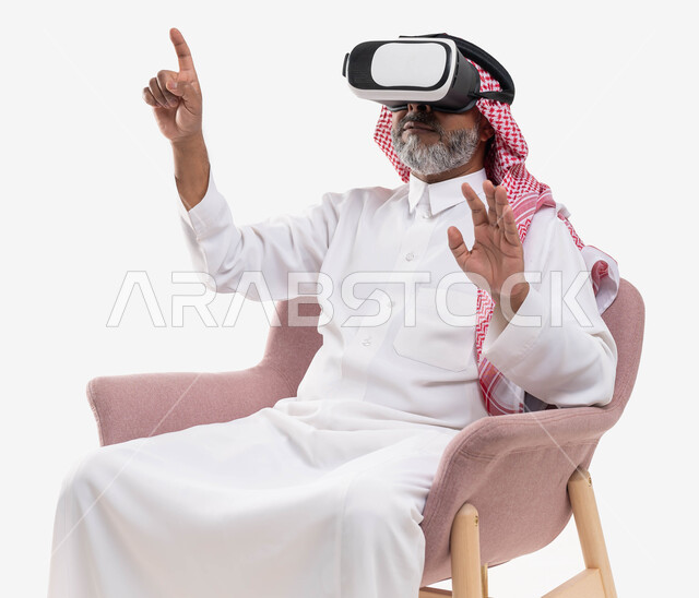 التفاعل والاندماج ومحاكاة العالم الخيالي, استخدام حاسة اللمس ومحاولة نقر شيء ما, مشاهدة الأفلام عبر نظارة الواقع الافتراضي في آر, بورتريه لرجل كبير بالسن عربي خليجي سعودي يرتدي الثوب التقليدي والنظارة ثلاثية الابعاد يرفع يديه للأعلى, خلفية بيضاء