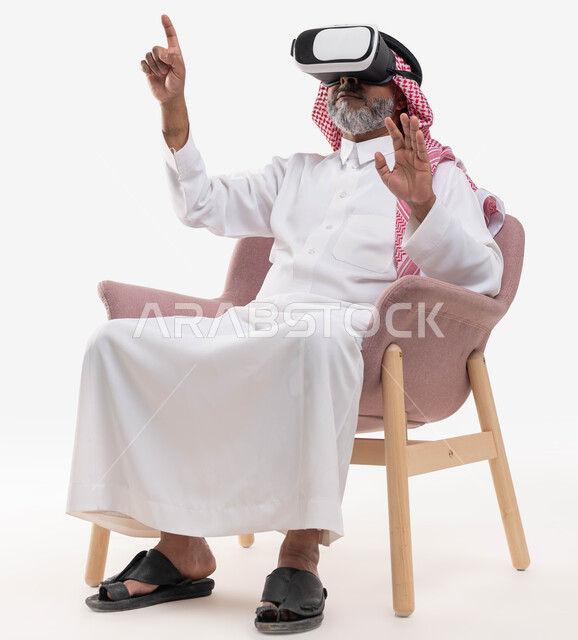 مشاهدة الأفلام عبر نظارة الواقع الافتراضي في آر, التفاعل والاندماج ومحاكاة العالم الخيالي, بورتريه لرجل كبير بالسن عربي خليجي سعودي يرتدي الثوب التقليدي والنظارة ثلاثية الابعاد يرفع يديه للأعلى, استخدام حاسة اللمس ومحاولة نقر شيء ما, خلفية بيضاء