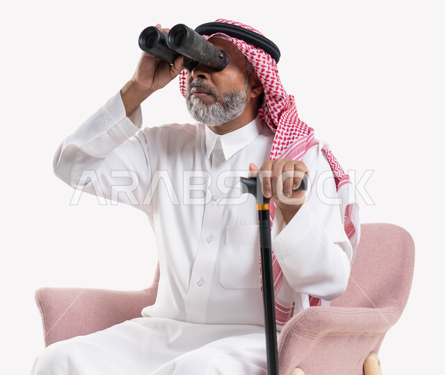 تحقيق الأهداف والطموحات المستقبلية, استخدام ناظور ثنائي العينين التلسكوب لرؤية الأشياء البعيدة, بورتريه لرجل كبير بالسن عربي خليجي سعودي يرتدي الثوب التقليدي والشماغ يمسك بيده العكاز وينظر إلى شيء ما عبر منظار الرؤية, حب الاستكشاف والمغامرة, خلفية بيضاء