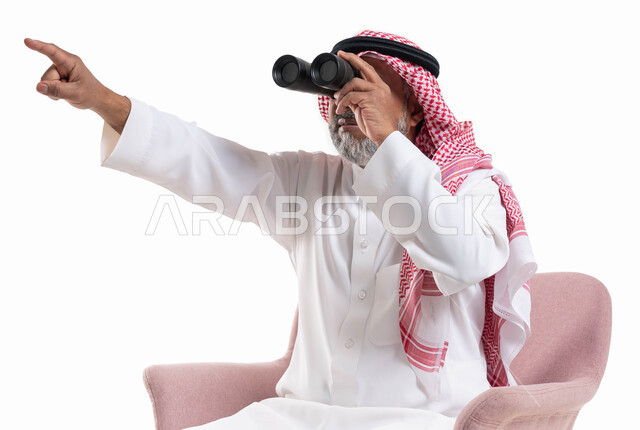 التخطيط المستقبلي للأهداف والطموحات, بورتريه لرجل شايب عربي خليجي سعودي يرتدي الثوب التقليدي والشماغ ينظر عبر منظار الرؤية ويشير بيده إلى شيء ما, رؤية الأشياء البعيدة عبر ناظور التلسكوب, حب الاستكشاف والمغامرة, خلفية بيضاء