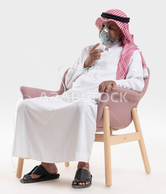تقديم الخدمات الصحية المنزلية للمريض، معالجة أمراض الربو المزمنة، المحافظة على ممر هوائي منتظم باستخدام جهاز التنفس الصناعي، بورتريه لرجل كبير بالسن عربي سعودي خليجي مريض يرتدي الشماغ والثوب التقليدي يجلس على الكرسي ويقوم باستنشاق أدوية الكحة، خلفية بيضاء