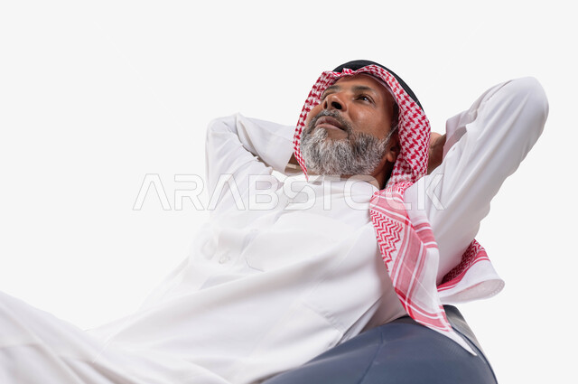 Expressions and gestures of thinking and wandering, looking at something, the concept of sitting and resting, a close-up portrait of an old Saudi Gulf Arab man wearing a shemagh and traditional thobe, sitting on a comfortable chair with his hands under his head, white background.