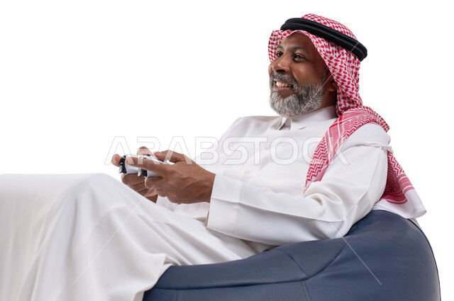 Spending a fun and entertaining time, interacting and merging with PlayStation games, modern electronic entertainment technologies, a close-up portrait of an elderly Saudi Arabian Gulf man wearing a shemagh and traditional dress, sitting on a comfortable chair holding a joystick in his hand, playing video games, white background.