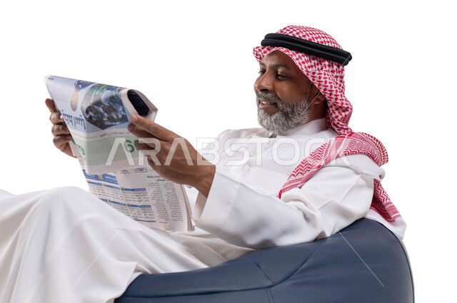تصفح الجرائد ومتابعة أحدث الأخبار، الإطلاع على المقالات والأحداث العالمية من خلال الصحائف, ممارسة هواية القراءة, بورتريه مقرب لرجل عربي خليجي سعودي كبير بالسن يرتدي الشماغ والثوب التقليدي يجلس على كرسي مريح يقوم بقراءة جريدة ورقيه، خلفية بيضاء