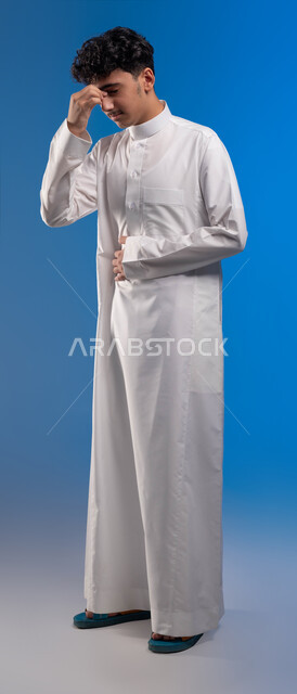 الشعور بالدوخة وعدم التوازن، الاحساس بالمرض و الصداع, بورتريه لشاب عربي سعودي خليجي يرتدي الزي التقليدي يضع يده على وجهه، التعب والإرهاق و الحاجه للعلاج, طلب المساعده للذهاب الى المستشفى, صورة للجسم بالكامل، خلفية زرقاء