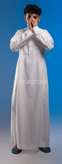 ايماءات تدل على العطاس, التهاب الجيوب الأنفية, الحاجة الى العلاج والدواء, بورتريه مقرب لشاب عربي خليجي سعودي يرتدي الزي التقليدي مصاب بنزلة برد, الشعور بالمرض و الزكام, صورة الجسم بالطول الكامل، خلفية زرقاء