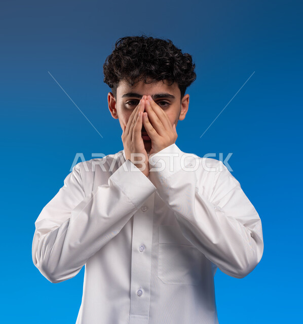 التهاب الجيوب الأنفية, الحاجة الى العلاج والدواء, ايماءات تدل على العطاس, بورتريه مقرب لشاب عربي خليجي سعودي يرتدي الزي التقليدي مصاب بنزلة برد, الشعور بالمرض و الزكام, خلفية زرقاء