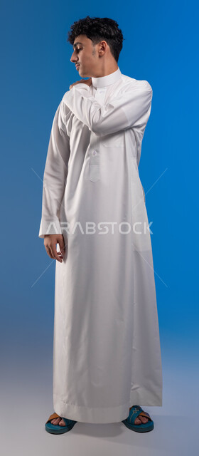 الحاجه للراحة و وضع خطة علاجية, شد عضلي في الرقبه ،التهاب العضلات والمفاصل، الإحساس بالتعب والإرهاق, بورتريه لشاب عربي سعودي خليجي يضع يده على رقبته بإيماءات الألم في الأكتاف، طلب المساعده للذهاب الى المستشفى، صورة الجسم بالكامل، خلفية زرقاء.