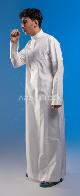 أعراض فايروس كورونا (كوفيد-19),  طلب المساعدة للذهاب الى الطبيب لوضع خطة العلاج, الاصابة بنزلة برد، بورتريه لشاب عربي خليجي سعودي يرتدي الزي التقليدي بإيماءات تدل على السعال و الألم, الشعور بالمرض و التعب والإرهاق, صورة الجسم بالكامل، خلفية زرقاء