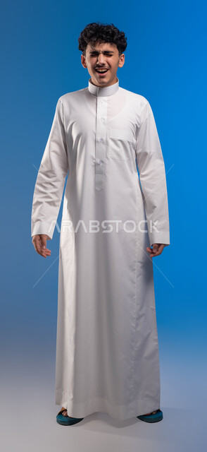 الحاجه للعلاج و طلب المساعده, الوقوف باستقامة والنظر إلى الكاميرا، الإحساس بالتعب والإرهاق, بورتريه مقرب لرجل عربي سعودي خليجي يرتدي الثوب التقليدي يصرخ بإيماءات الوجع, الشعور بالصداع و ألم بالرأس, صورة الجسم بالطول الكامل، خلفية زرقاء .