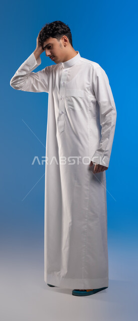 الحاجه للعلاج و طلب المساعده, الإحساس بالدوار والتعب والإرهاق, بورتريه لرجل عربي سعودي خليجي يرتدي الثوب التقليدي يضع يده على رأٍسه بإيماءات الوجع, الشعور بالصداع و ألم بالرأس, صورة الجسم بالطول الكامل، خلفية زرقاء .