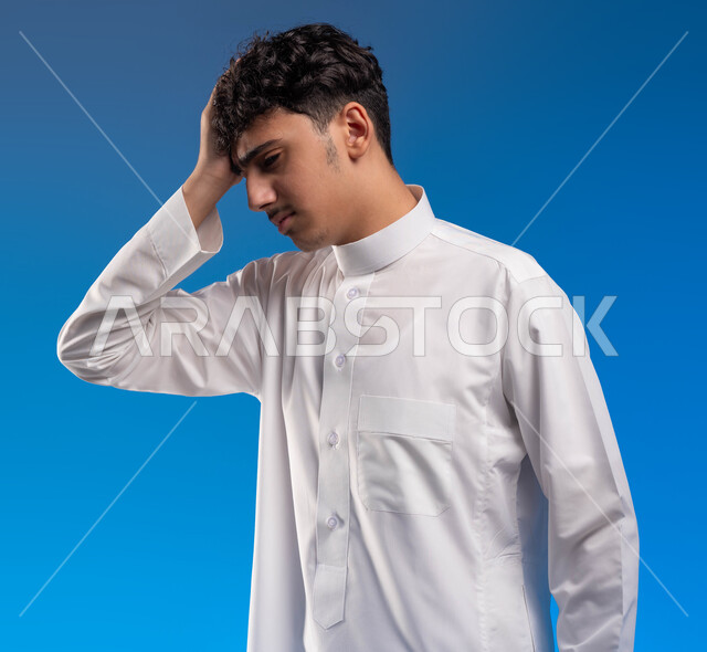 الإحساس بالدوار والتعب والإرهاق, بورتريه مقرب لرجل عربي سعودي خليجي يرتدي الثوب التقليدي يضع يده على رأٍسه بإيماءات الوجع, الشعور بالصداع و ألم بالرأس, الحاجه للعلاج و طلب المساعده , الحاجة للراحة والنوم، خلفية زرقاء .