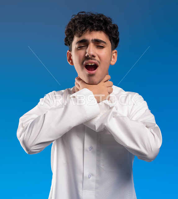 إيماءات صعوبة التنفس والتعب والألم، بورتريه مقرب لشاب عربي سعودي خليجي يرتدي الثوب التقليدي يضع يديه على حلقه يشعر بالاختناق، الاصابة بنزلة برد والتهاب الحلق، المرض الشديد والسعال، العدوى بفايروس كورونا، خلفية زرقاء .