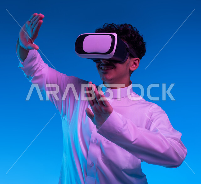 Interaction and simulation of the imaginary world, a close-up portrait of a Saudi Gulf Arab boy wearing a traditional dress and virtual reality glasses with self-defense gestures, merging and trying to catch something, modern techniques and technological devices, blue background