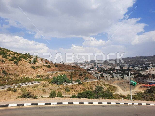 White clouds and clouds in the sky of the Kingdom, public roads and streets in the villages and neighborhoods of Al-Baha Governorate, trees and green plants in broad daylight, homes and residential buildings, natural mountain peaks and heights, tourist places in Saudi Arabia.