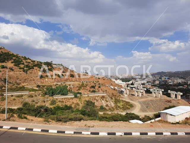 Trees and green plants on the mountains in broad daylight, public roads and streets in Al-Baha Governorate, white clouds and clouds in the sky of the Kingdom, mountain peaks and heights, landscapes in Saudi Arabia