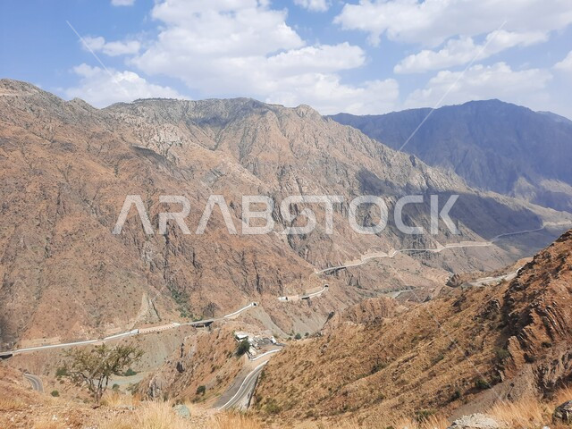 Landscapes and famous tourist places in Saudi Arabia, terrain and rock formations in the peaks and heights of the Kingdom, construction of paved roads and streets in the mountains of Al-Baha Governorate, a winding asphalt road between high mountain ranges.