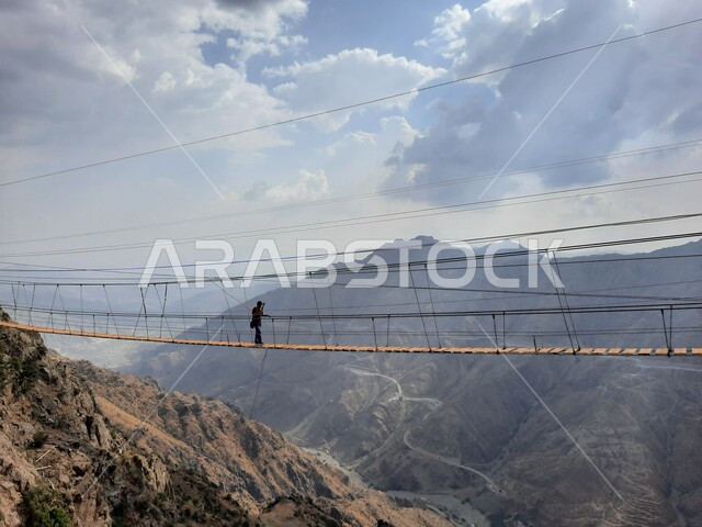 القمم والمرتفعات الجبلية الصخرية في الباحة، أنشطة ترفيهية ممتعة في الأماكن السياحية السعودية، سائح يمارس النشاطات الحركية المسلية وسط المناظر الطبيعة في منتزهات وحدائق المملكة، فعالية السير على الجسر الخشبي المعلق في حديقة الأمير حسام