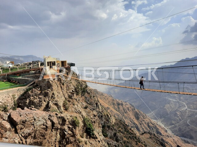 فعالية السير على الجسر الخشبي المعلق في حديقة الأمير حسام، أنشطة ترفيهية ممتعة في الأماكن السياحية السعودية، سائح يمارس النشاطات الحركية المسلية وسط المناظر الطبيعة في منتزهات وحدائق المملكة، القمم والمرتفعات الجبلية الصخرية في الباحة