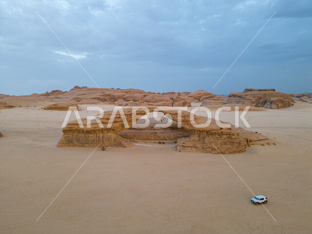 القمم والمرتفعات الجبلية الطبيعية وسط البيئة الرمليه، التكوينات والتشكيلات الصخرية في صحراء محافظة العلا، صخرة القوس الشهيرة في المناطق الصحراوية في المملكة العربيه السعودية، معالم اثرية تاريخية قديمة ، اماكن سياحية مشهورة، منظر السماء المليئة بالغيوم البيضاء