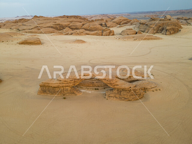 Ancient historical monuments, a picture from above of the famous Arc Rock in the desert areas of Saudi Arabia, natural mountain peaks and heights in the sandy environment, famous tourist places, rock formations and formations in the desert of Al-Ula Governorate, a view of the sky filled with white clouds.