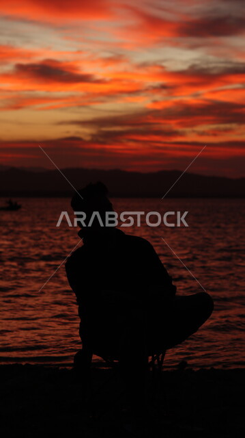 الشعور بالوحدة والاكتئاب، الحاجة إلى الاسترخاء والتأمل أمام البحر وقت غروب الشمس، صورة ظليه لشاب عربي خليجي سعودي يجلس على شاطئ البحر ،الاستمتاع بأوقات الفراغ في المناطق الساحليه السياحيه, سيلوليت