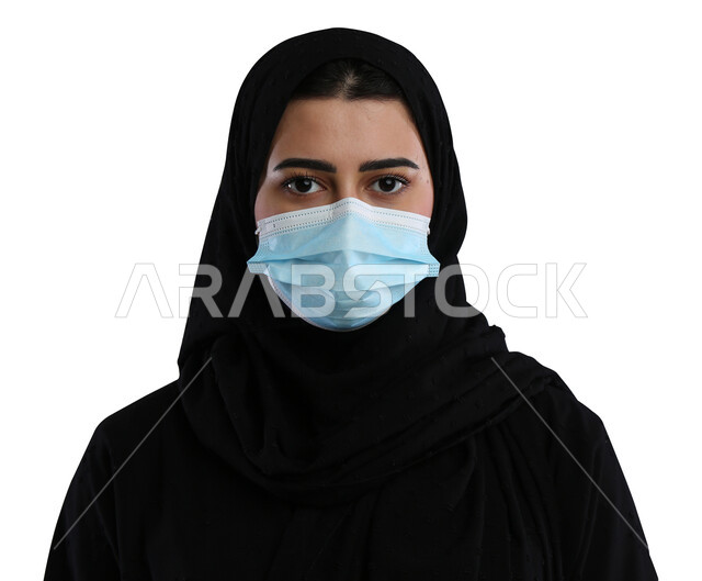 الحفاظ على السلامة و تجنب انتشار العدوى من كوفيد 19 ،الاحتراز والوقاية من فايروس كورونا ، بورتريه مقرب لإمرأة عربية سعودية خليجية محجبة ترتدي الكمامة وتنظر إلى الكاميرا , خلفية بيضاء