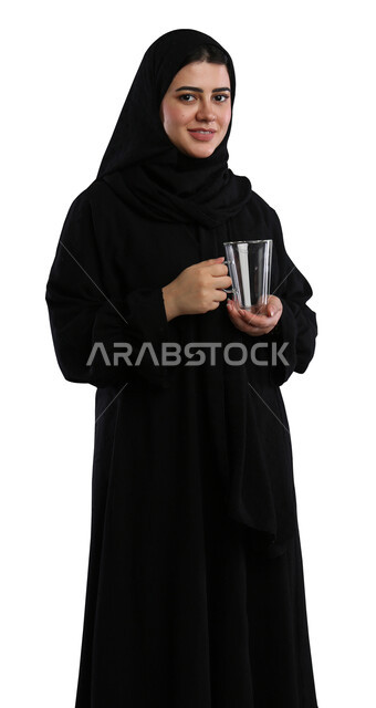 تناول المشروبات الساخنه الشهيه، منتجات محلية وطنية سعودية، بورتريه لامراة عربيه خليجية سعودية مبتسمة محجبة ترتدي العباءة السوداء تحمل بيدها كوب من القهوة، النظر الى الكاميرا بإيماءات السرور، مفهوم الاهتمام بالمظهر الخارجي، خلفية بيضاء