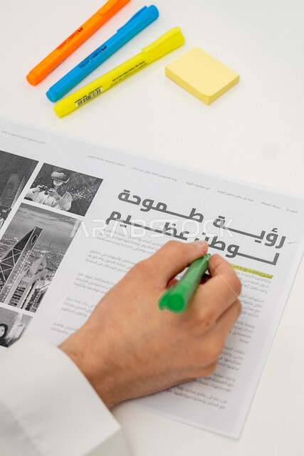 بناء واقع أفضل بسواعد أبناء الوطن، صورة مقربة ليد رجل عربي خليجي سعودي يحمل بيده قلم ويشير إلى عبارة رؤية طموحة لوطن عظيم، رؤية مستقبلية سعودية 2030 ، الاهتمام بالتطور والنمو وتحقيق اهداف السعودية ، أقلام ملونة على خلفية بيضاء