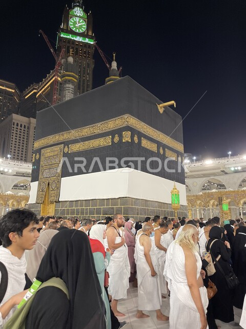 أداء مناسك الحج والعمرة، العبادة والتقرب إلى الله في الأماكن والمعالم الدينية الإسلامية، الحجاج المسلمين يطوفون حول الكعبة المشرفة في مكة المكرمة الحرم المكي الشريف في مكة المكرمة بالمملكة العربية السعودية، مبنى برج الساعة الملكي.