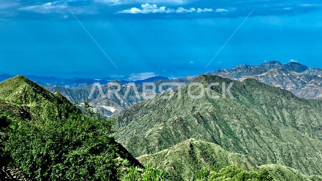 سلسلة جبال تنومة في منطقة عسير جنوب غرب المملكة العربية السعودية، الأشجار والنباتات الخضراء على القمم والمرتفعات الجبلية، السماء المليئة بالغيوم والسحب الكثيفة، أماكن ومعالم طبيعية سياحية.