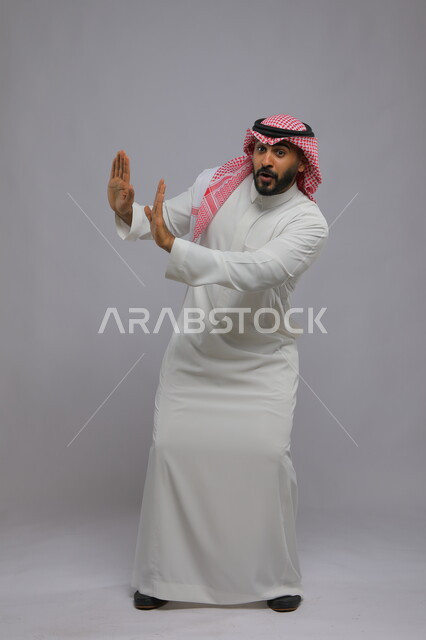 رقصات سعودية تقليدية شعبية, العراقة والأصالة والتراث السعودي, بورتريه لرجل عربي خليجي سعودي يرتدي الثوب التقليدي والشماغ يرفع يديه للأعلى, التعابير والرقصات بالاحتفالات والمناسبات في المملكة, صورة الجسم بالطول الكامل, خلفية رمادية