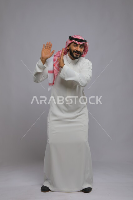 رقصات سعودية تقليدية شعبية, العراقة والأصالة والتراث السعودي, بورتريه لرجل عربي خليجي سعودي يرتدي الثوب التقليدي والشماغ يرفع يديه للأعلى, التعابير والرقصات بالاحتفالات والمناسبات في المملكة, صورة الجسم بالطول الكامل, خلفية رمادية